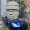 テスラって恨まれてるの？メキシコの彫刻家が「モデル3を巨大石頭で潰す作品」を公開